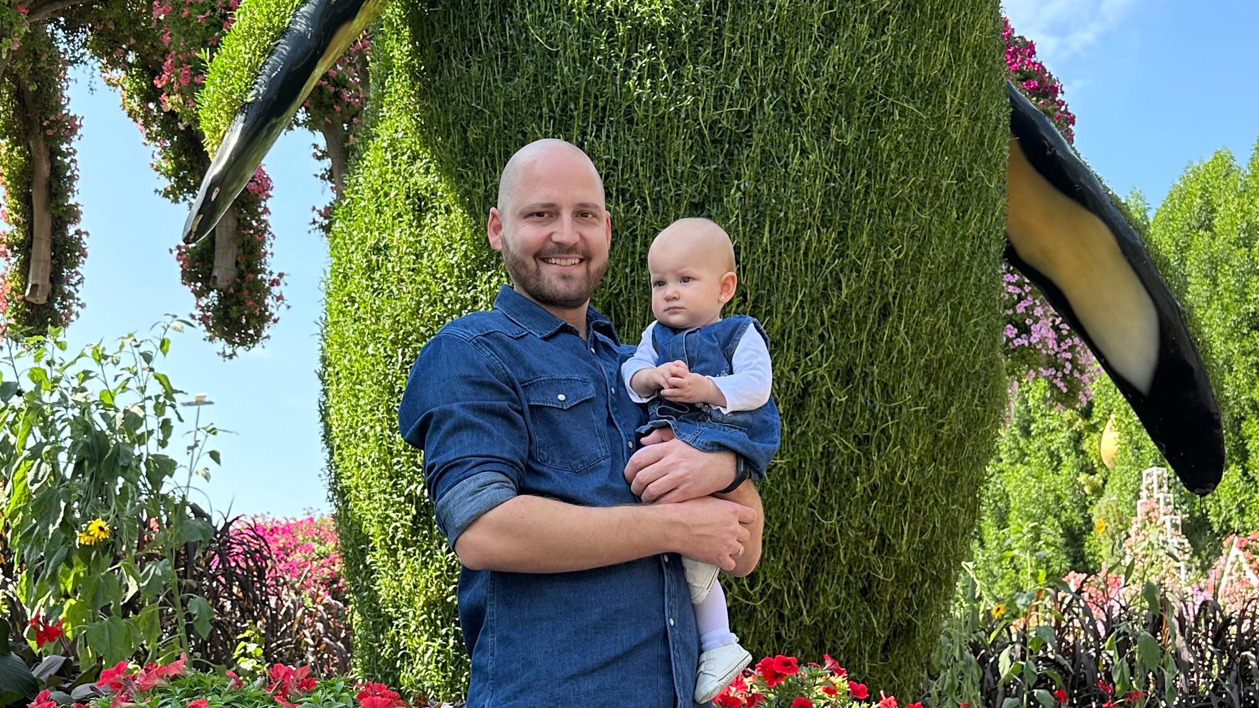 Smilling father with baby girl in front of a giant penguin statue